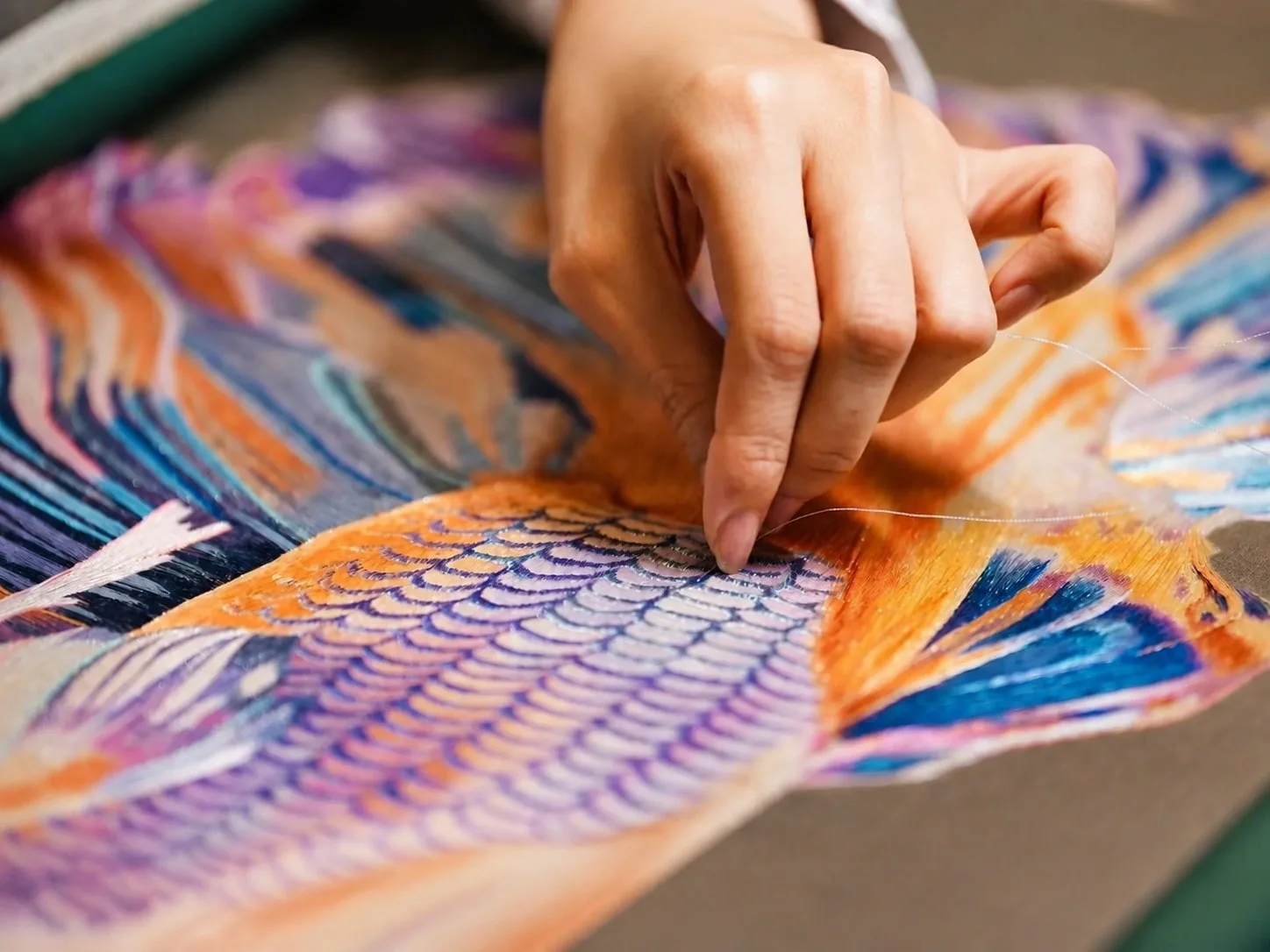 A Chaozhou embroiderer's hands working gold thread at the frame
