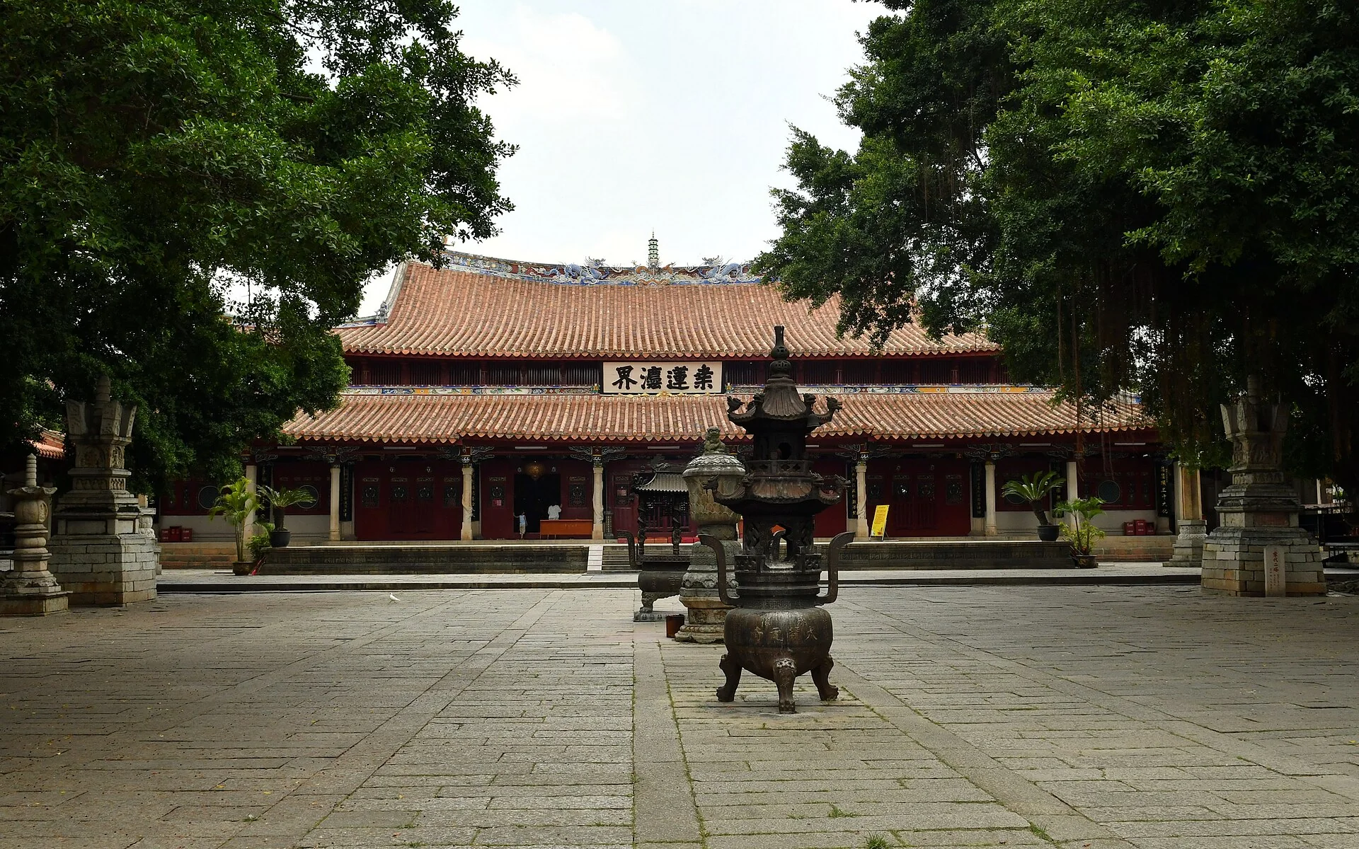 Quanzhou Kaiyuan Temple: Mahavira Hall with its Sang Lian Fa Jie plaque, framed by ancient banyans